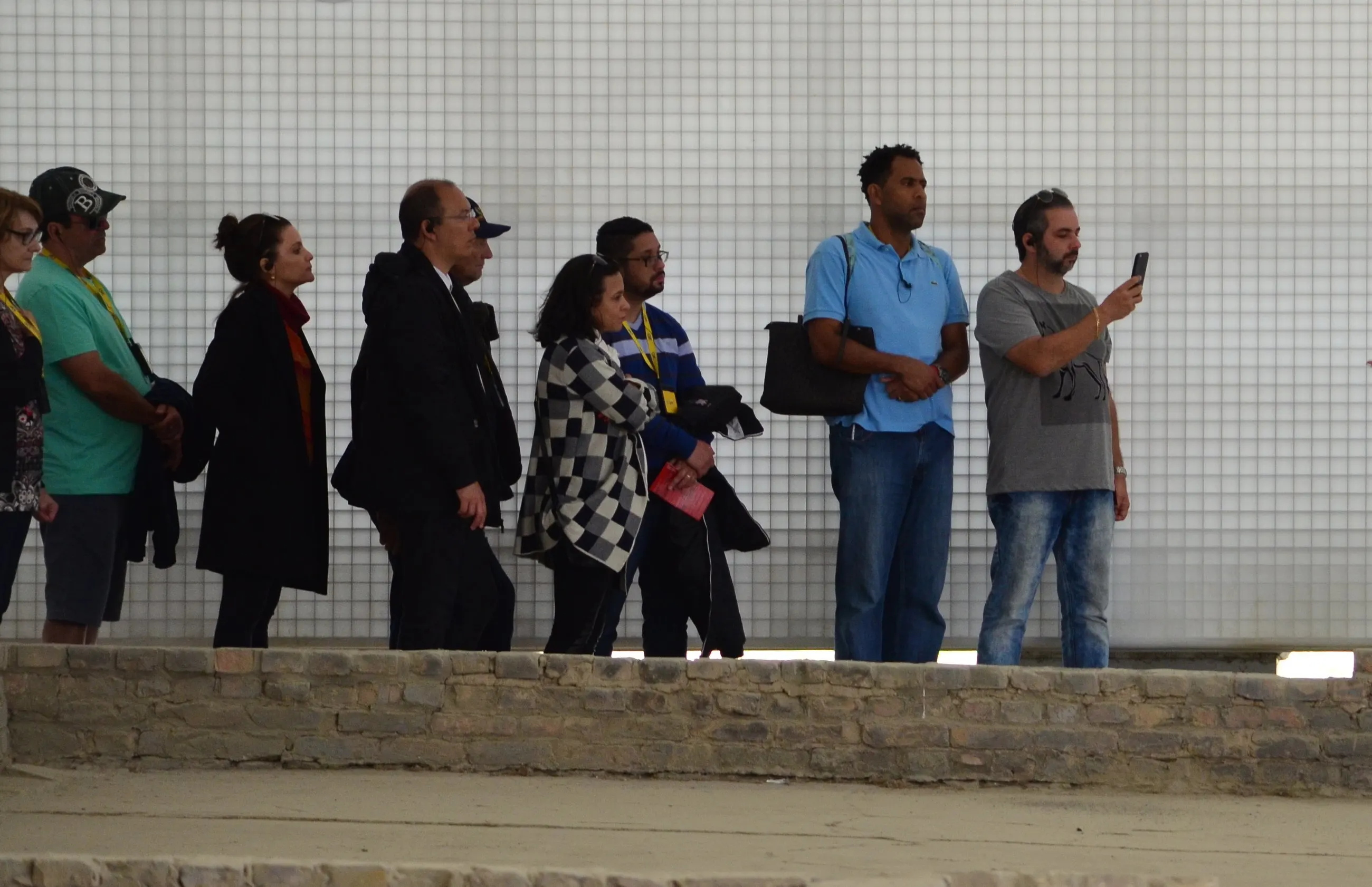 Grupo diante de um muro branco no memorial de Sachsenhausen, ouvindo a explicação de Marta